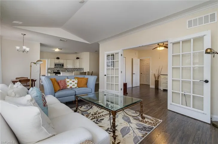 Living room featuring lofted ceiling, dark wood-laminate flooring, ornamental molding, ceiling fan with notable chandelier, and french doors