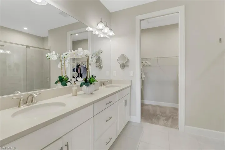 Primary bathroom featuring a spacious closet, double vanity, a shower stall, and tile floors; pocket door on closet