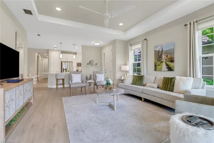 Living area with light wood-style flooring, a raised ceiling, plenty of natural light, and recessed lighting
