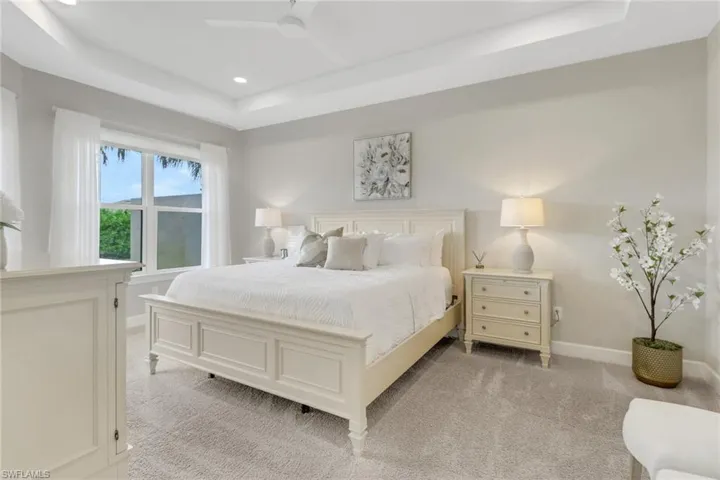 Primary bedroom featuring a king sized bed, raised ceiling, light carpet, recessed lighting, and ceiling fan