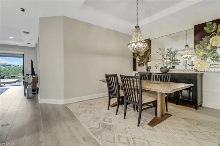Dining room featuring a chandelier, a raised tray ceiling, light wood-style floors, and mirrored wall