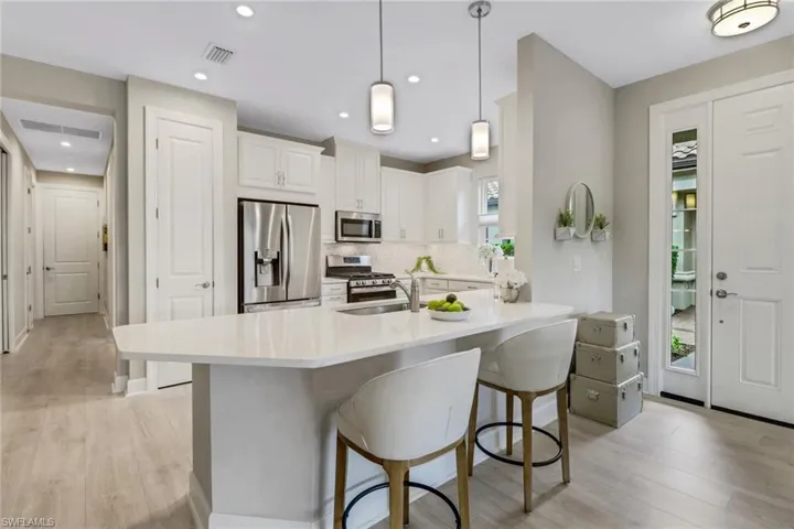 Kitchen featuring appliances with stainless steel finishes, gas range, light wood-style floors, a kitchen bar, decorative backsplash, and quartz countertops