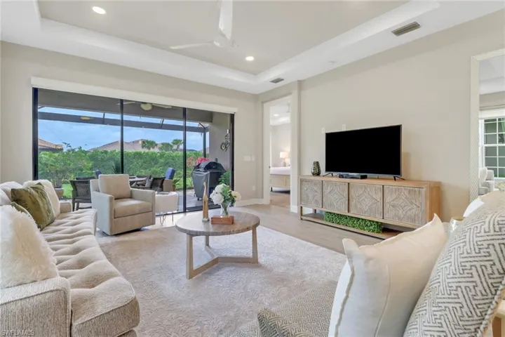 Living area featuring a tray ceiling, healthy amount of natural light, recessed lighting, a ceiling fan, and wood-style  floors.  Beautiful slider glass doors to lanai!