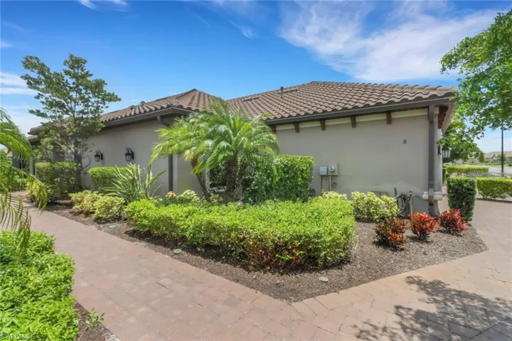 View of side of home featuring stucco siding, lush landscaping and a tiled roof