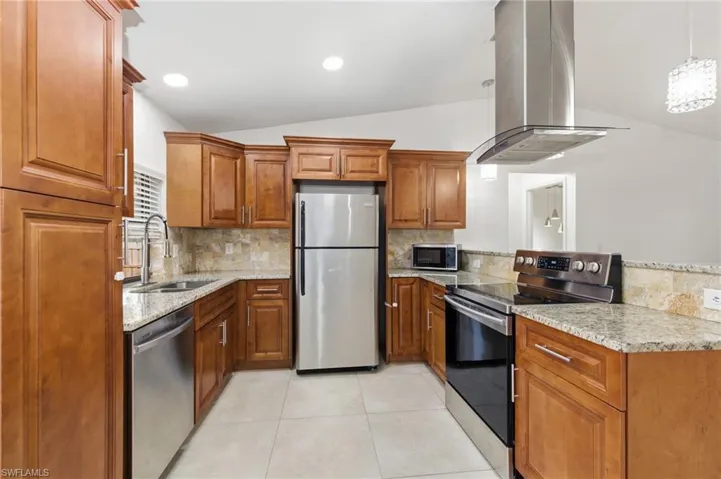 Kitchen featuring stainless steel appliances, wood finish cabinets, light stone counters, decorative backsplash, and lofted ceiling