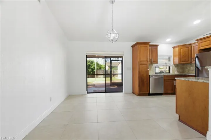 Kitchen with wood finish cabinets, stainless steel appliances, vaulted ceiling, light stone counters, and tasteful backsplash