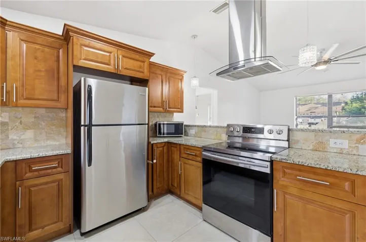 Kitchen with stainless steel appliances, island exhaust hood, wood finish cabinets, and light stone countertops