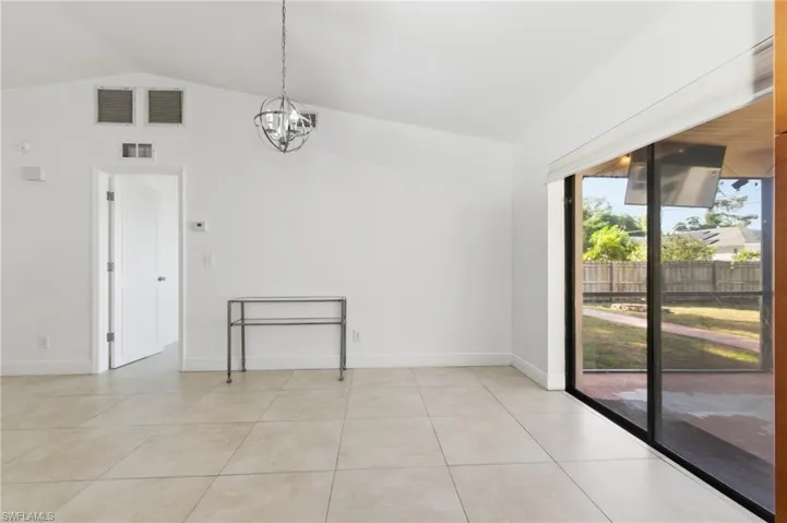 Empty room with vaulted ceiling, a chandelier, and light tile patterned floors