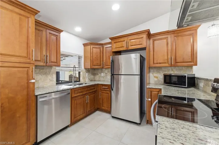 Kitchen featuring lofted ceiling, wood finish cabinetry, stainless steel appliances, ventilation hood, and decorative backsplash