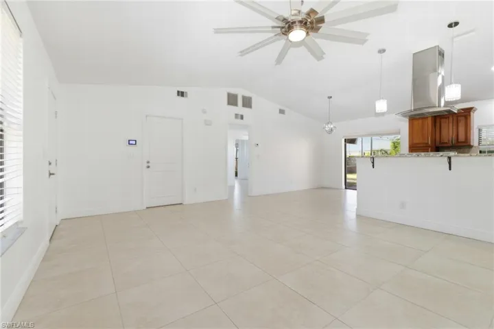 Unfurnished living room featuring light tile patterned floors, vaulted ceiling, a ceiling fan, and hanging lights