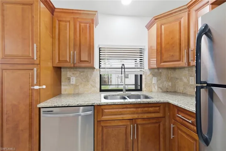 Kitchen with stainless steel appliances, light stone countertops, wood finish cabinets, and backsplash