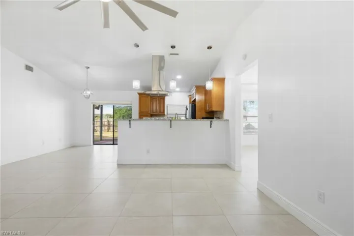 Kitchen with wood finish cabinetry, decorative light fixtures, a breakfast bar area, a peninsula, and island exhaust hood