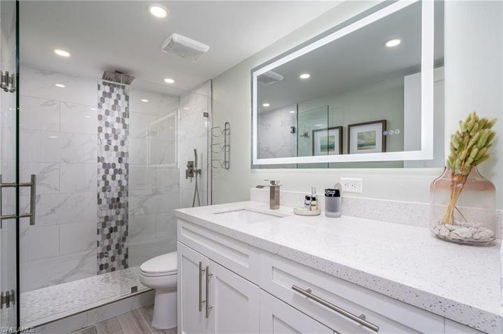 The bathroom features a sleek, glass walk-in shower, ensured to always provide hot shower thanks to the tankless water heater.  Backlit mirror with multiple settings. This bathroom is both functional and stylish.