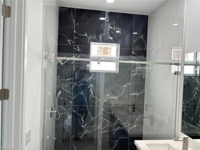 Full bath with a marble finish shower, healthy amount of natural light, and vanity