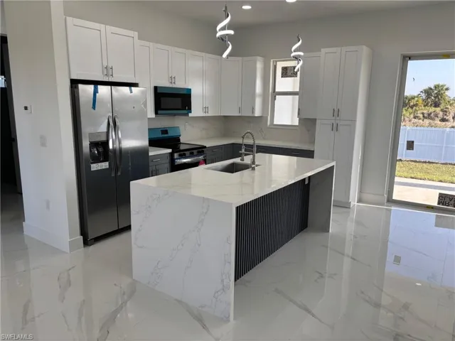 Kitchen featuring stainless steel appliances, a sink, light stone countertops, tasteful backsplash, and a center island with sink