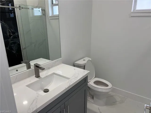 Full bath with toilet, marble look tiles, healthy amount of natural light, and a marble finish shower