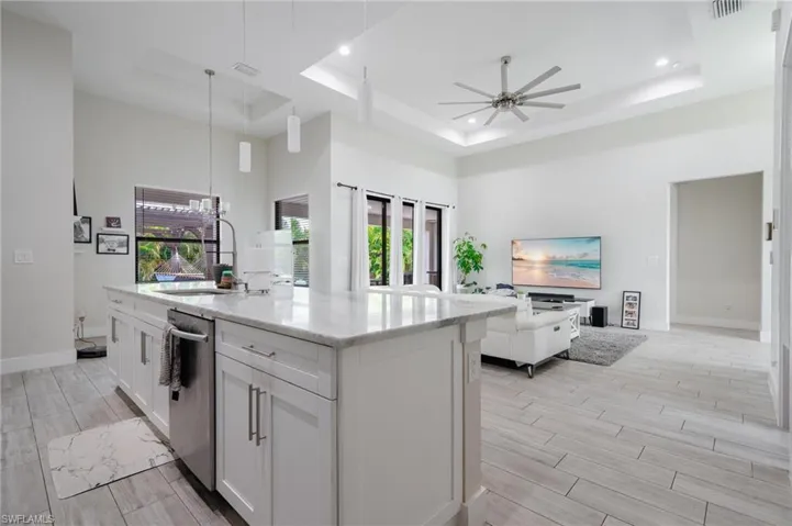 Kitchen with white cabinetry, ceiling fan, a raised ceiling, and a center island with sink