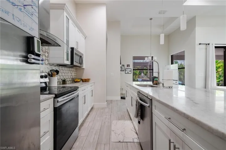 Kitchen with white cabinets, decorative backsplash, wall chimney exhaust hood, sink, and appliances with stainless steel finishes