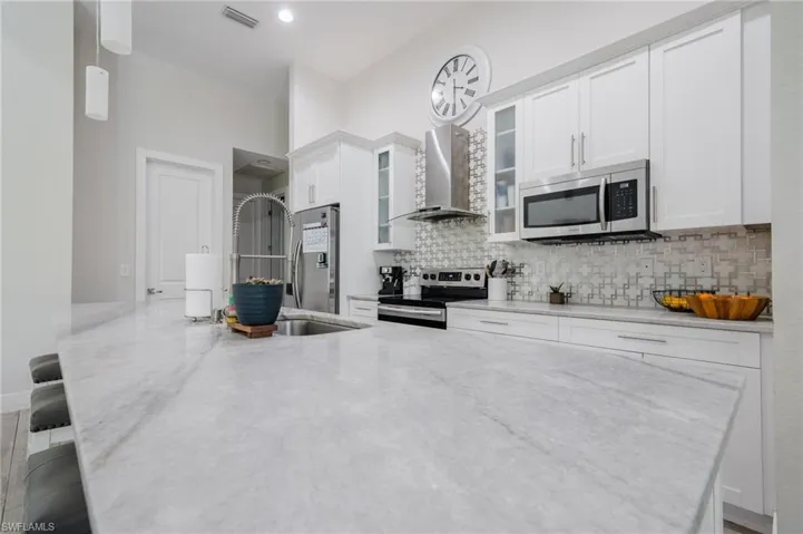 Kitchen with white cabinetry, tasteful backsplash, wall chimney exhaust hood, light stone countertops, and appliances with stainless steel finishes