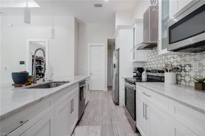 Kitchen with white cabinetry, tasteful backsplash, wall chimney range hood, stainless steel appliances, and hanging light fixtures