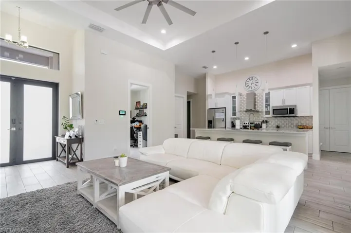 Living room featuring ceiling fan with notable chandelier and a raised ceiling