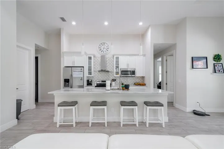 Kitchen with wall chimney range hood, light stone counters, stainless steel appliances, and a breakfast bar