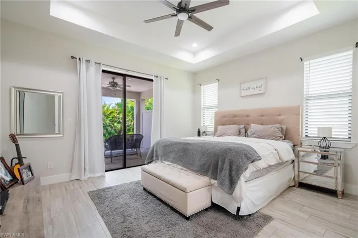 Bedroom featuring ceiling fan, access to outside, light wood-type flooring, and a tray ceiling