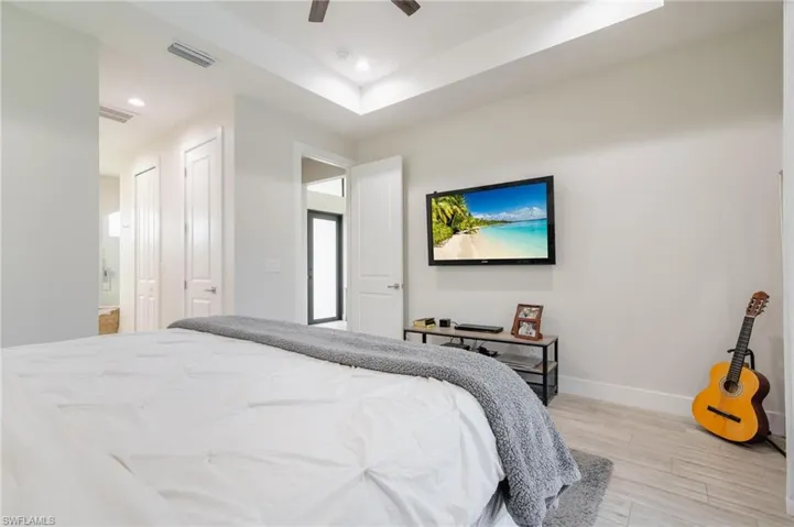Bedroom featuring ensuite bath, a tray ceiling, ceiling fan, and light hardwood / wood-style floors