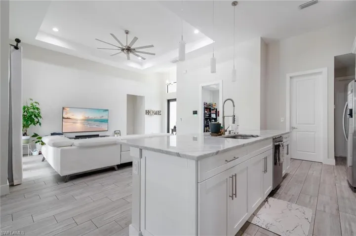 Kitchen with sink, hanging light fixtures, a raised ceiling, and a kitchen island with sink
