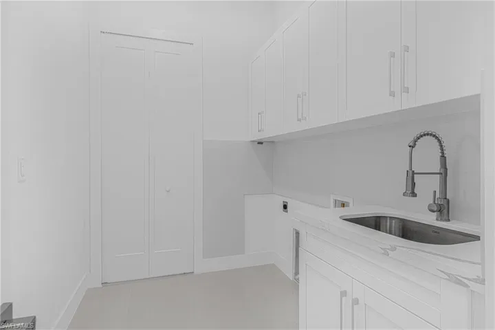 Laundry area featuring washer hookup, light tile patterned floors, cabinet space, and a sink