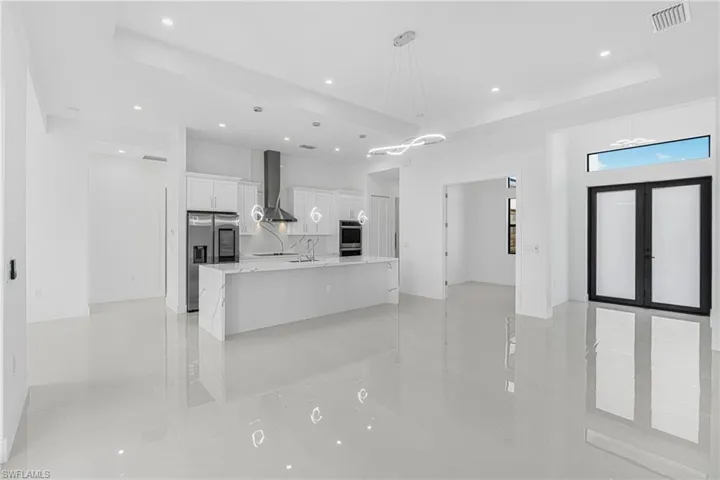 Kitchen featuring visible vents, stainless steel fridge with ice dispenser, white cabinetry, a raised ceiling, and wall chimney range hood