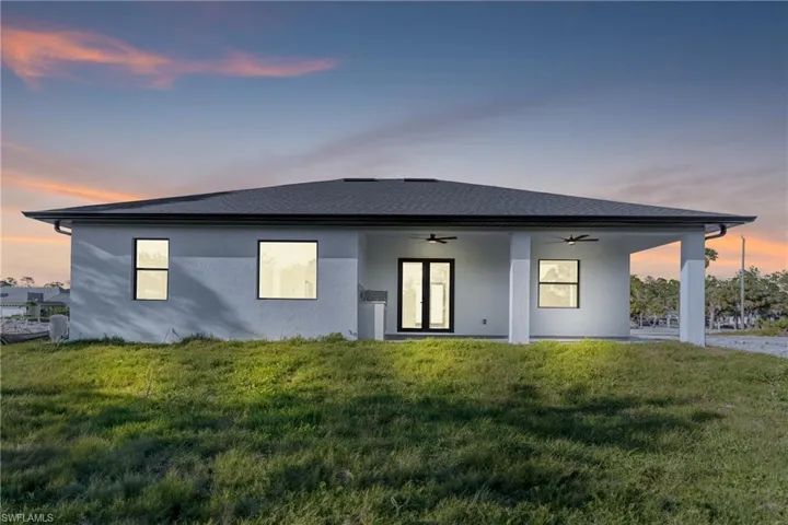Rear view of property featuring stucco siding, a lawn, ceiling fan, and roof with shingles