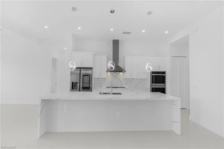 Kitchen featuring backsplash, appliances with stainless steel finishes, a large island, white cabinetry, and wall chimney exhaust hood