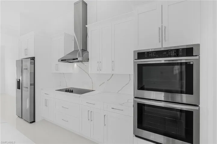 Kitchen with tasteful backsplash, white cabinetry, appliances with stainless steel finishes, wall chimney range hood, and light stone countertops