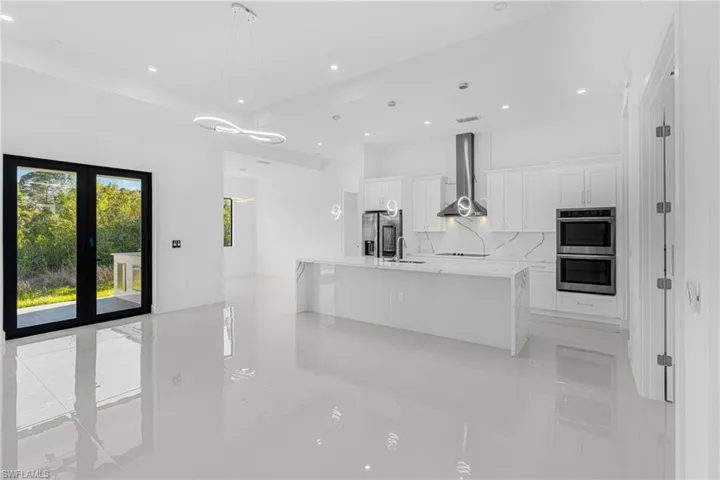 Kitchen with a sink, stainless steel appliances, white cabinetry, and wall chimney range hood