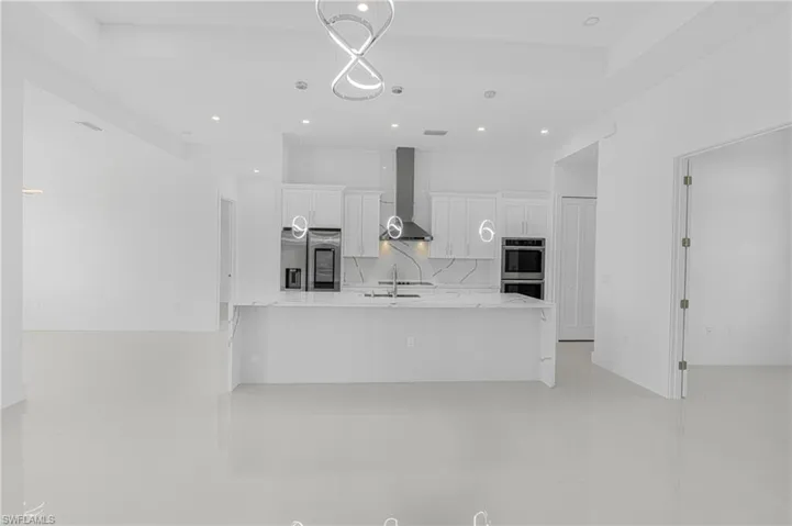 Kitchen featuring light stone counters, stainless steel appliances, white cabinets, wall chimney range hood, and tasteful backsplash
