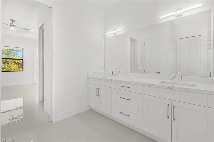 Bathroom with double vanity, a ceiling fan, baseboards, and a sink