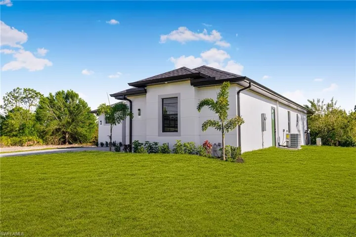 View of side of property featuring stucco siding, a yard, central AC unit, and driveway