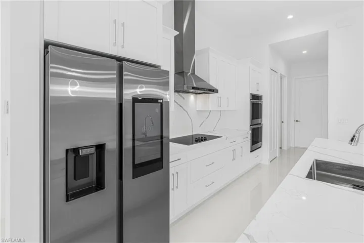 Kitchen with a sink, light stone counters, appliances with stainless steel finishes, white cabinets, and wall chimney range hood