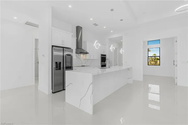 Kitchen featuring visible vents, stainless steel appliances, white cabinets, wall chimney range hood, and a large island with sink