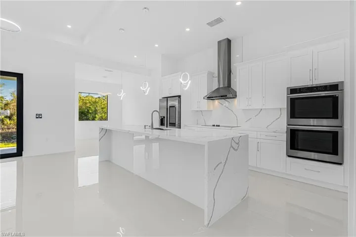 Kitchen with stainless steel appliances, white cabinetry, a large island with sink, and wall chimney range hood