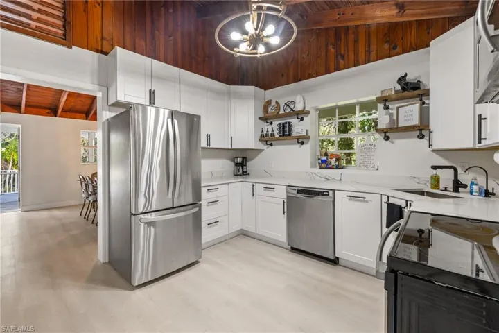 Kitchen with a wooden ceiling with exposed beams, open shelves, stainless steel appliances, light stone countertops, and white cabinetry