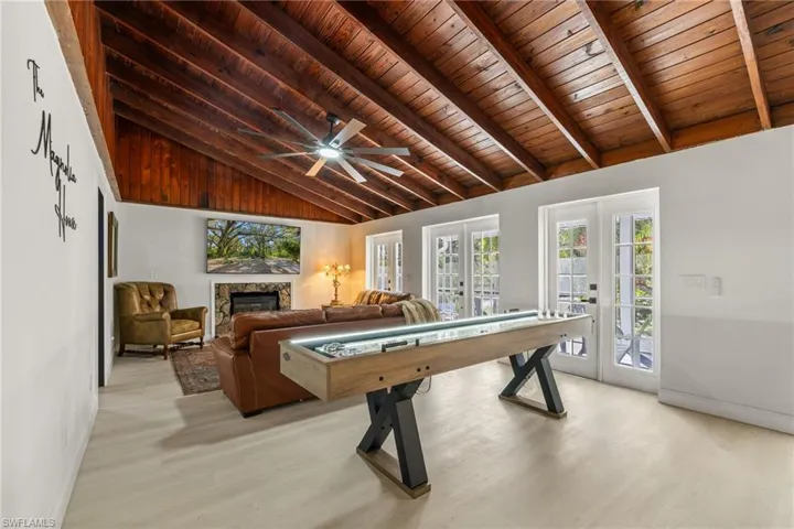 Game room featuring french doors, a wooden ceiling with exposed beams, healthy amount of natural light, a glass covered fireplace, and light wood finished floors