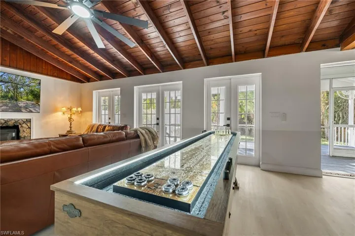 Game room featuring wood ceiling, plenty of natural light, light wood finished floors, french doors, and a stone fireplace