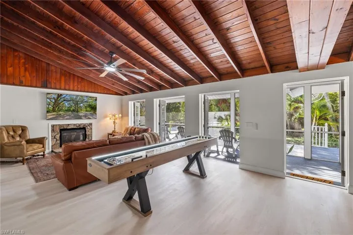 Playroom with wood ceiling, a stone fireplace, light wood-style flooring, ceiling fan, and vaulted ceiling