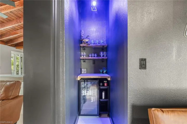 Indoor dry bar with a wood ceiling with exposed beams, a textured wall, and beverage cooler