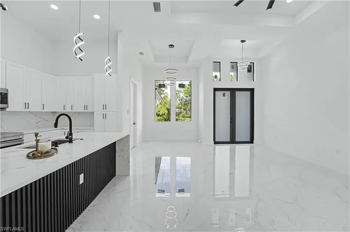 Open-concept interior featuring high ceilings, white cabinetry, a kitchen island with a waterfall countertop, and large format polished tile flooring