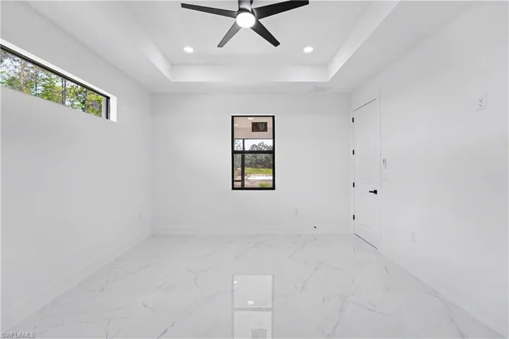 White large format tile flooring, tray ceiling with recessed lighting, black ceiling fan, and modern black-framed windows