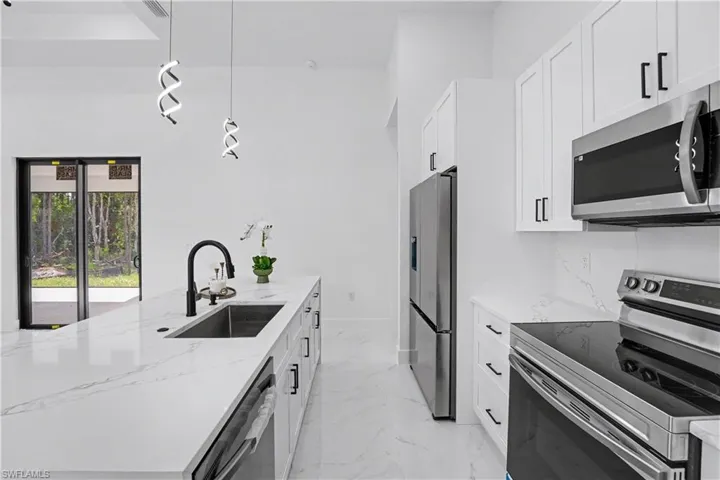 Kitchen island with integrated sink and matte black faucet, white cabinetry with black hardware, stainless steel appliances, and white marble-finish countertops