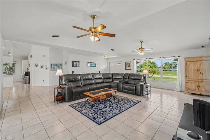 Spacious living area featuring tiled flooring, vaulted ceilings, and multiple ceiling fans